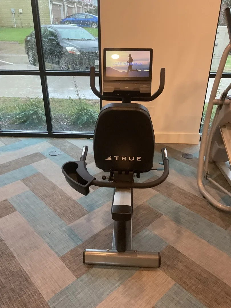 True recumbent bike with touchscreen console, positioned facing the window wall