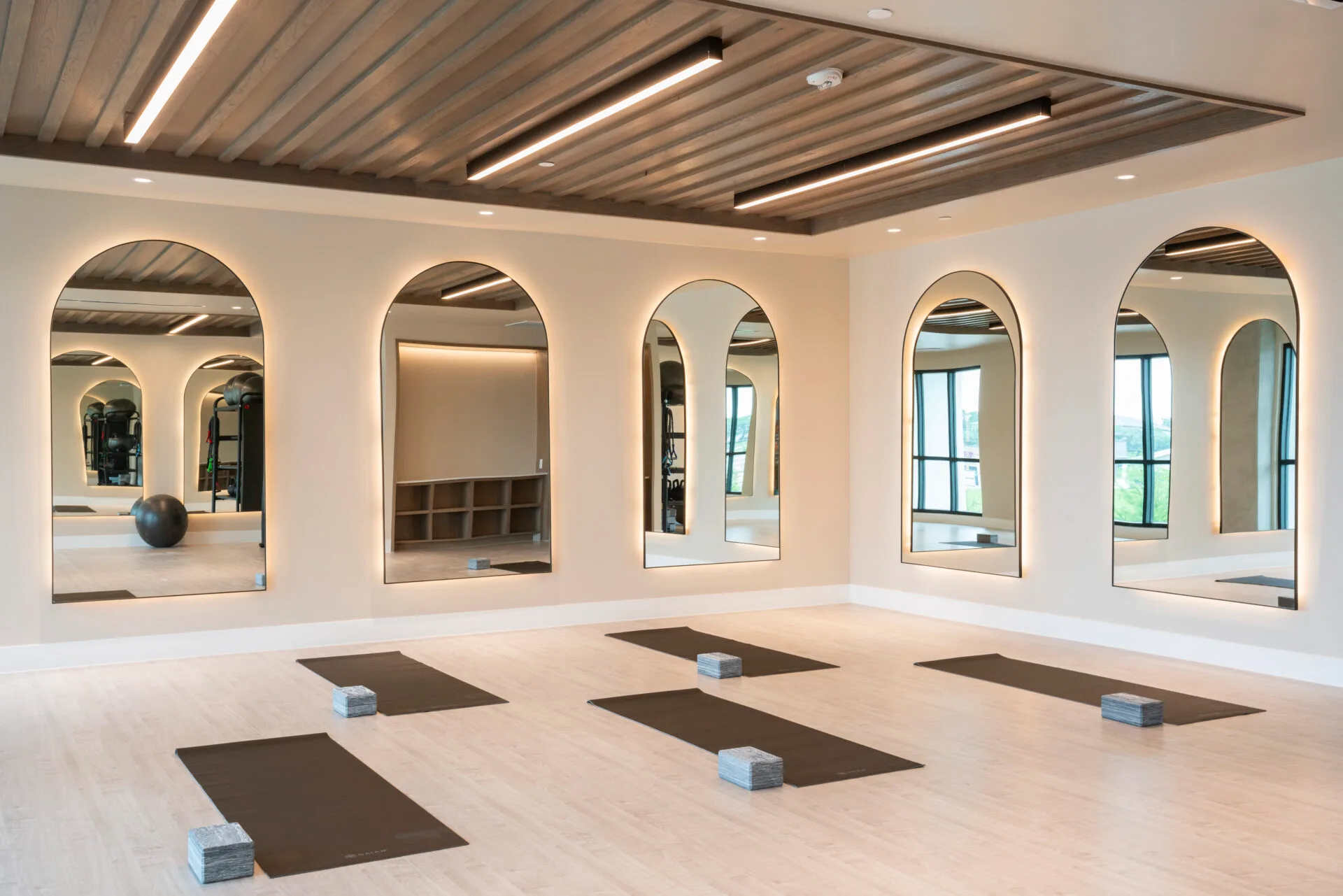 Mirrored mind-body studio with yoga mats and blocks under backlit arched mirrors