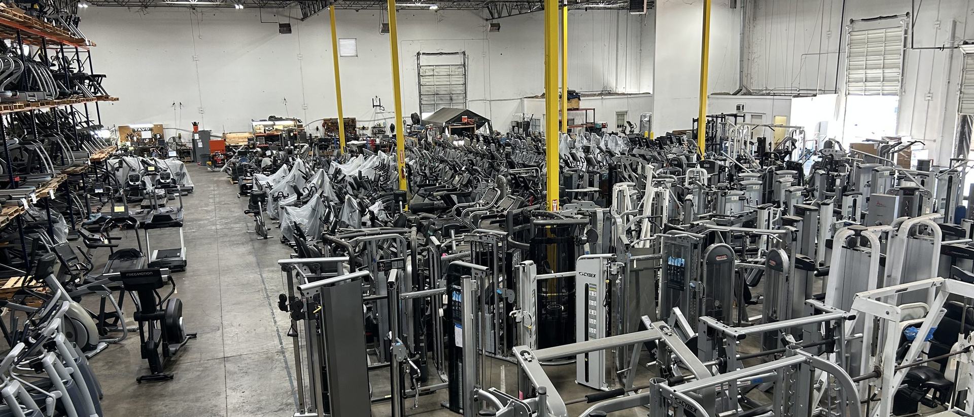 Rows of pre-owned commercial treadmills, ellipticals and strength equipment racked floor-to-ceiling in the Discount Online Fitness warehouse